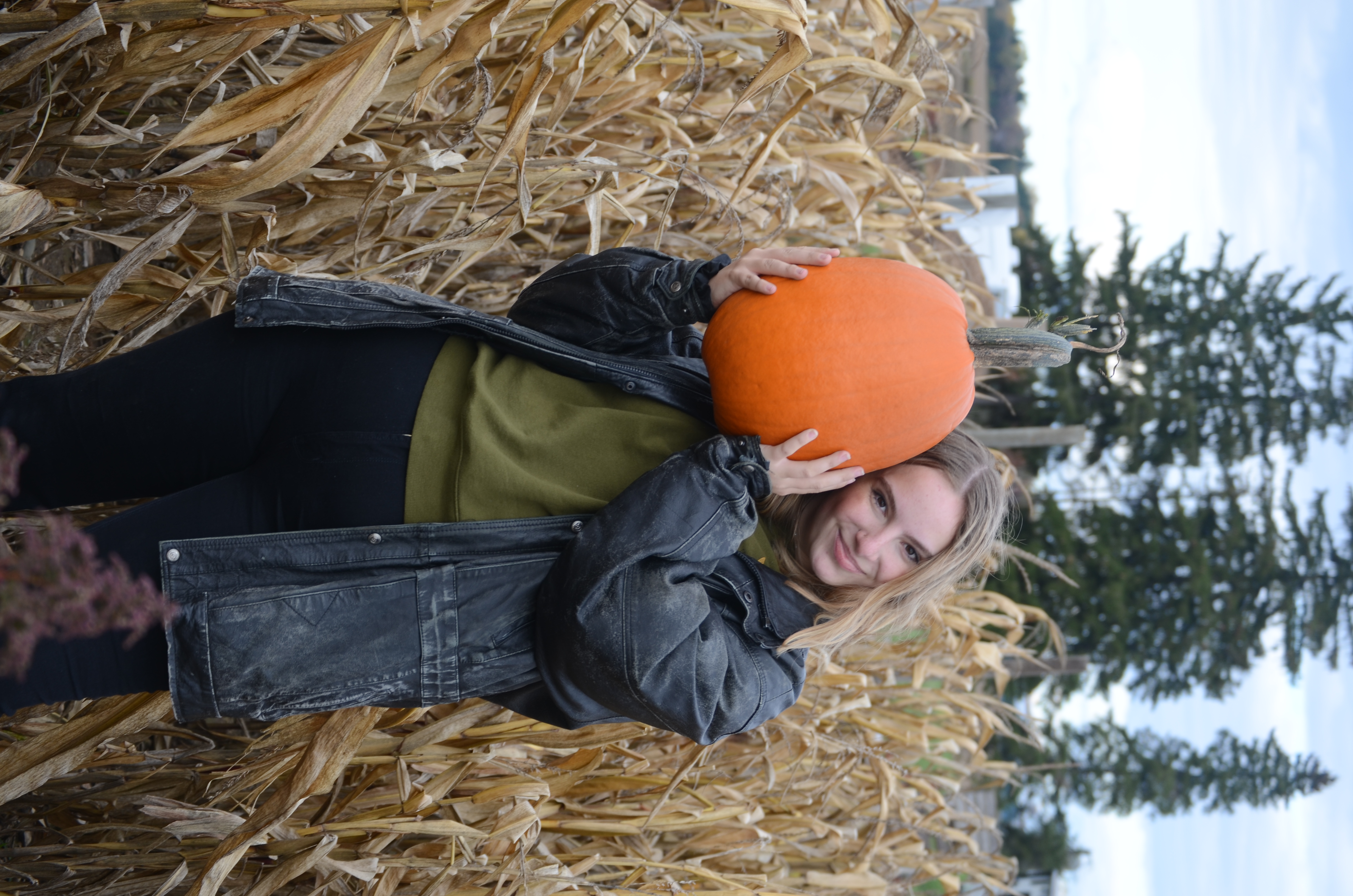 Blonde haired girl (ME!) smiling in a corn field while holding a pumpkin.