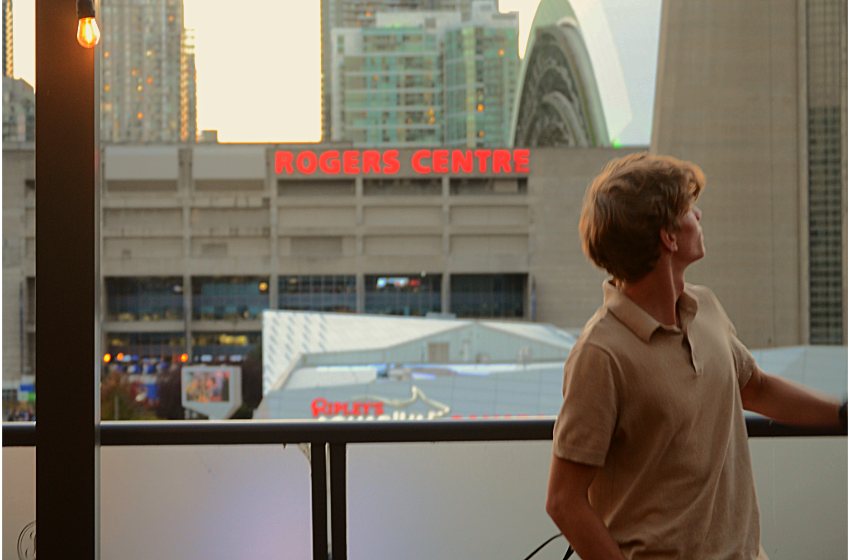 Blonde-haired man looking to up at the CN Tower behind him.