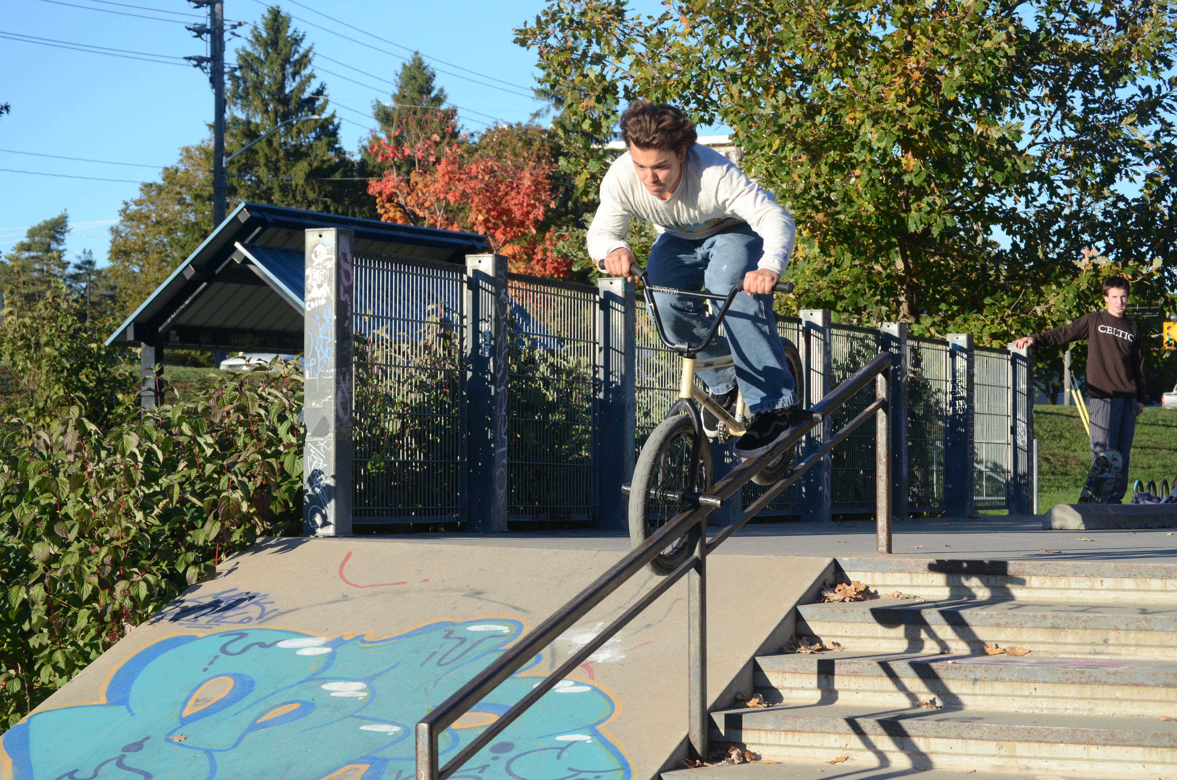 Dark-haired man grinding a rail at the skatepark on a BMX bike.