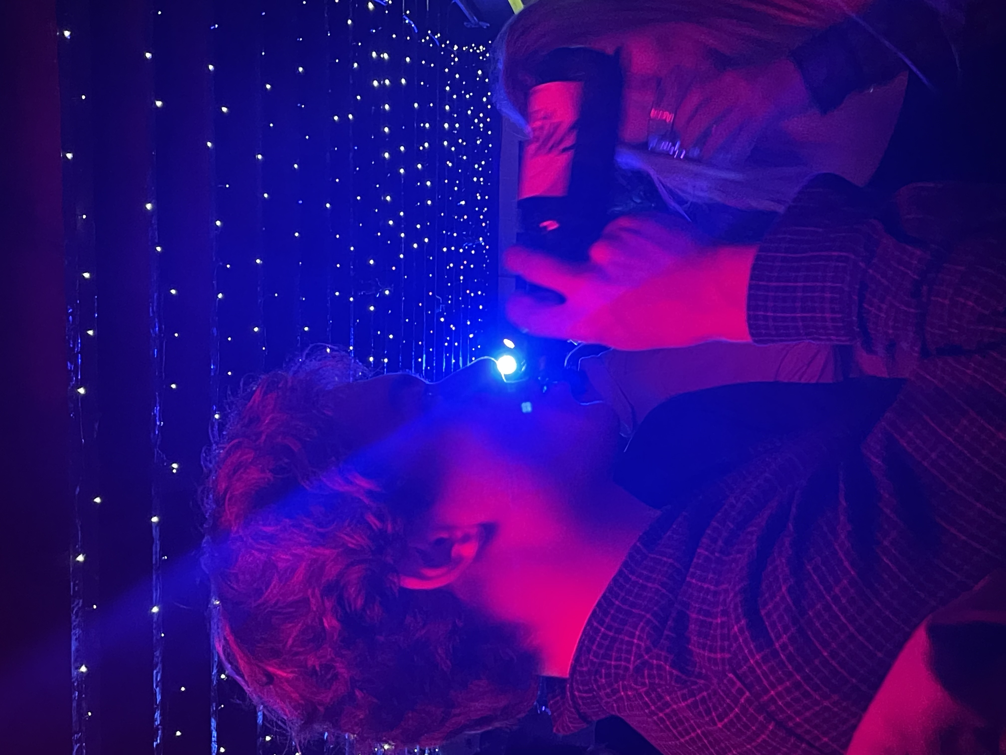 Man with brown hair drinking a beer in a purple and blue lit club.