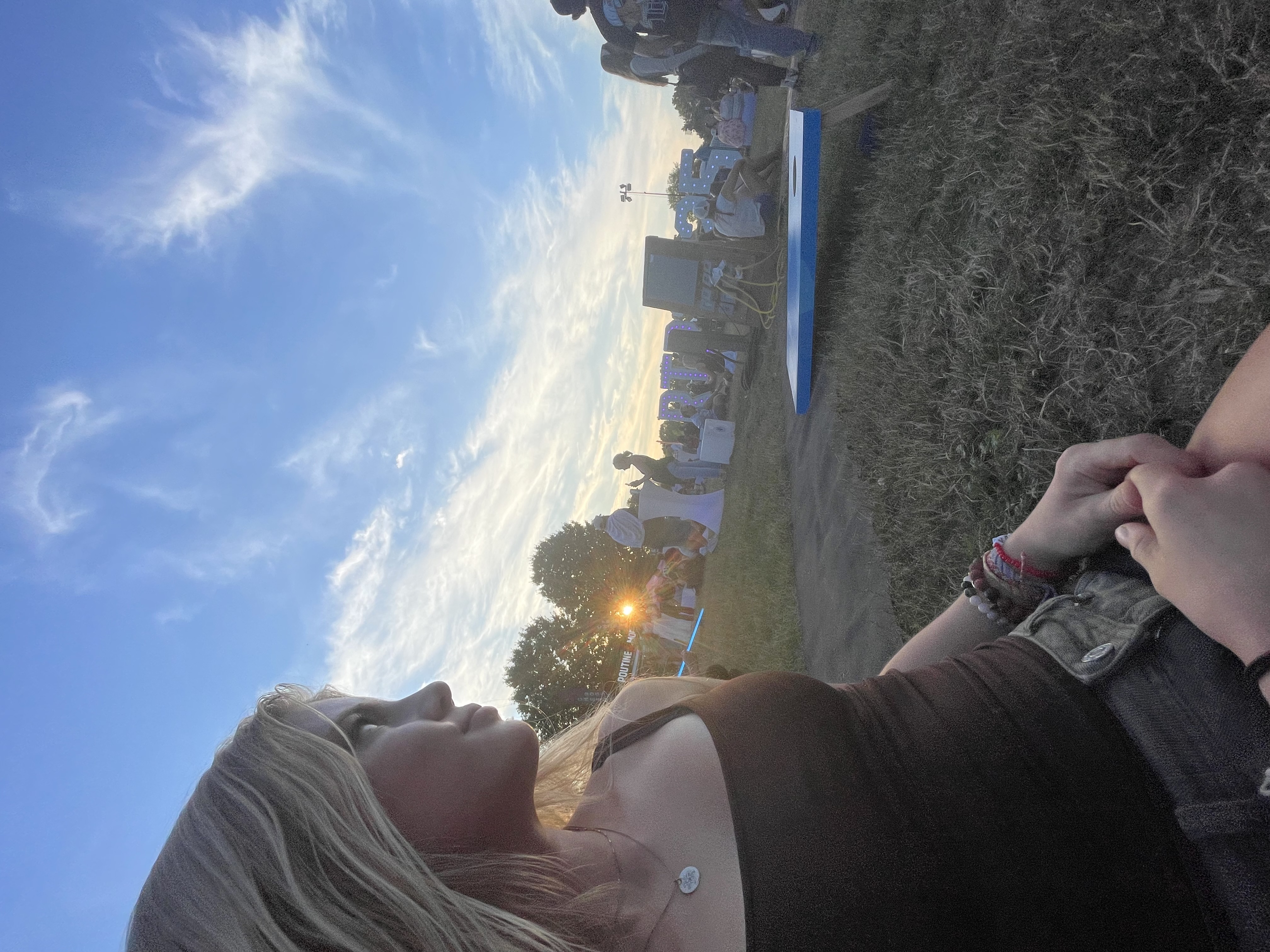 A blonde-haired girl looking behind her at the orange sunset at a music festival.