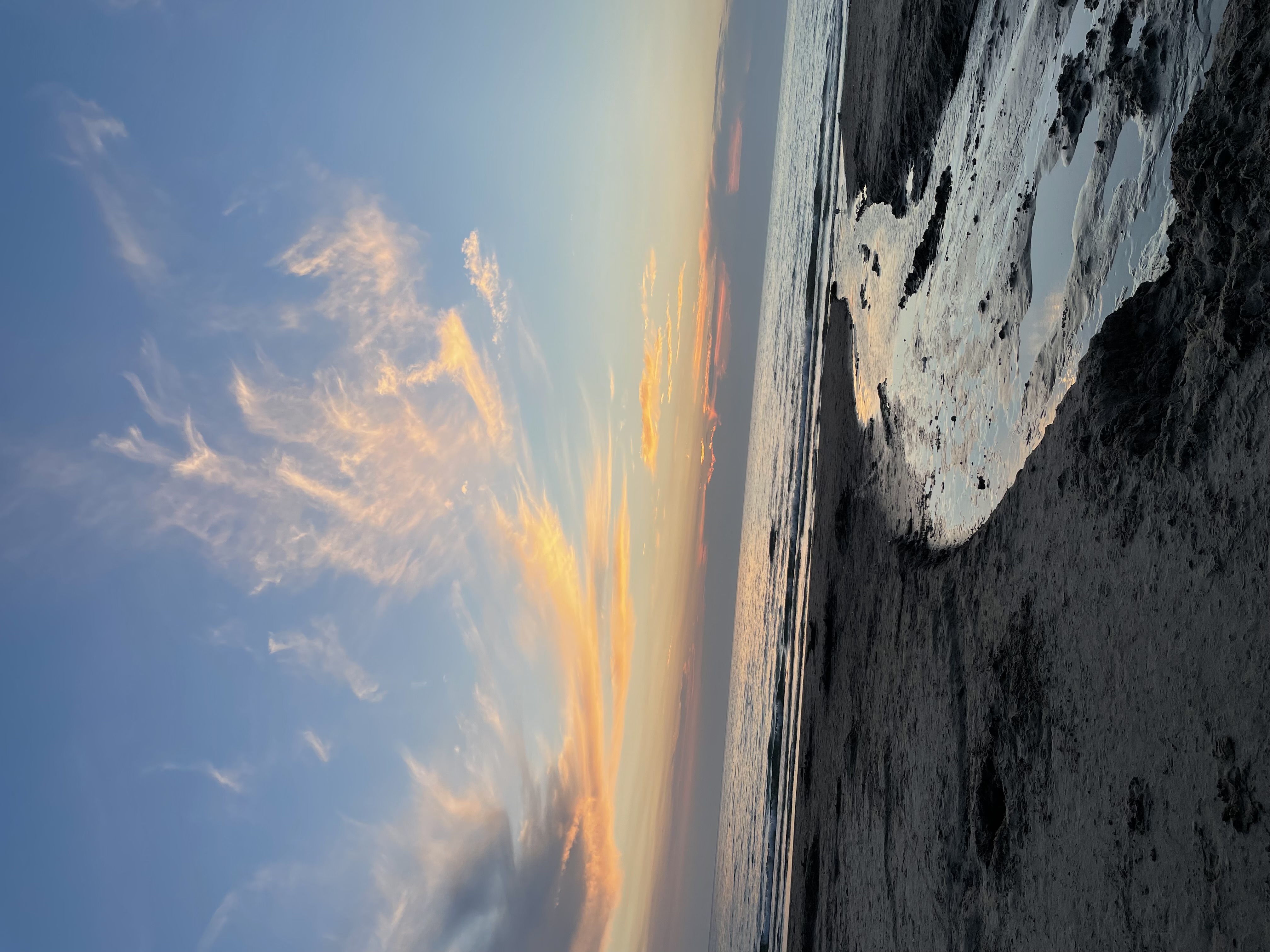 A sand beach at dusk with a sunset starting on the horizon.