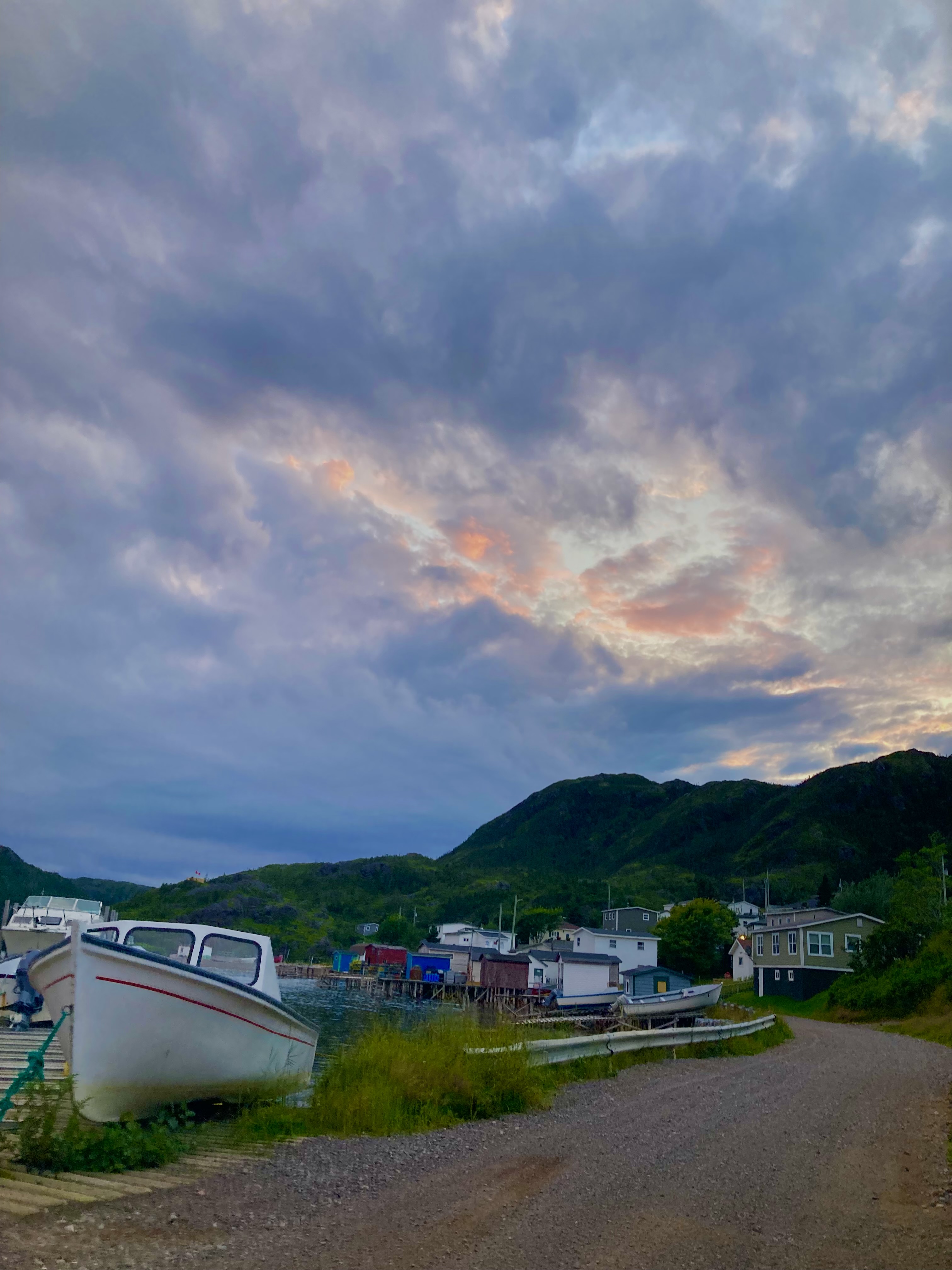 A white boat next to a dirt path with a sunset in the background.