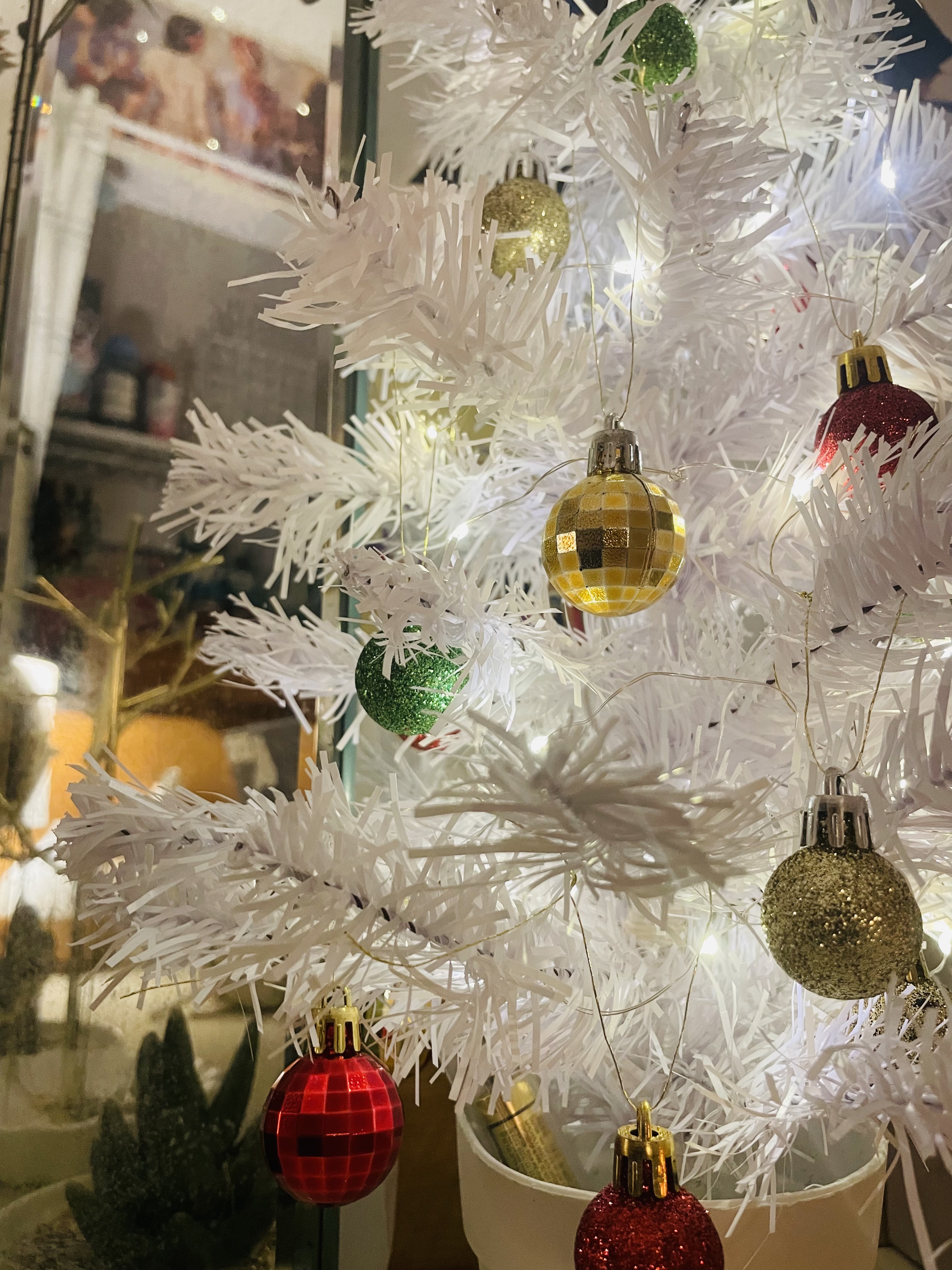 White Christmas tree with red and green ornaments and sparkling gold lights.