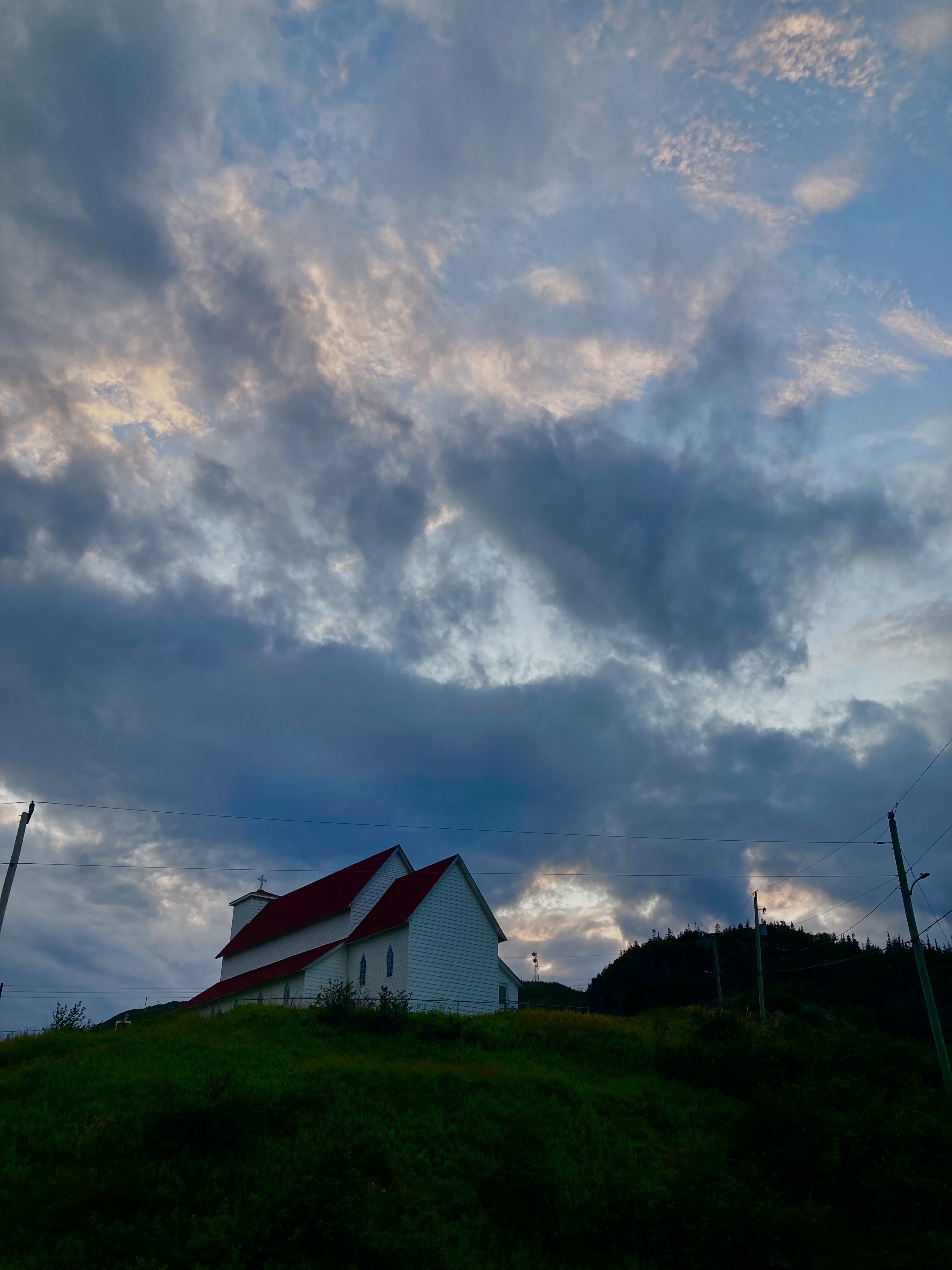 A white church with a red roof on a hill with a sunset behind it.