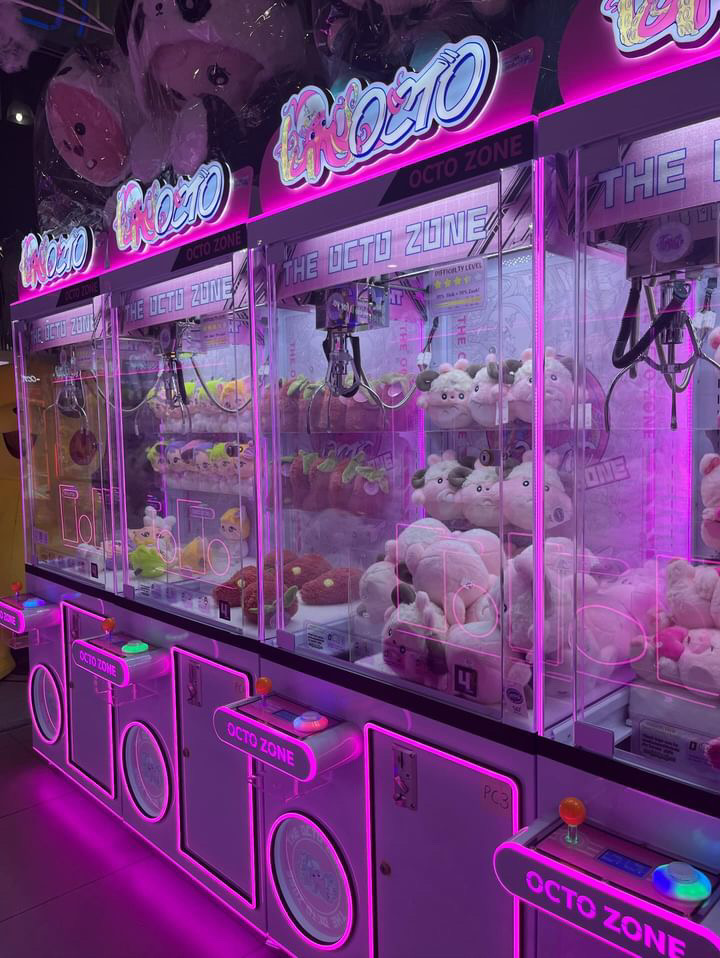 A row of pink claw machines with bright pink lights.