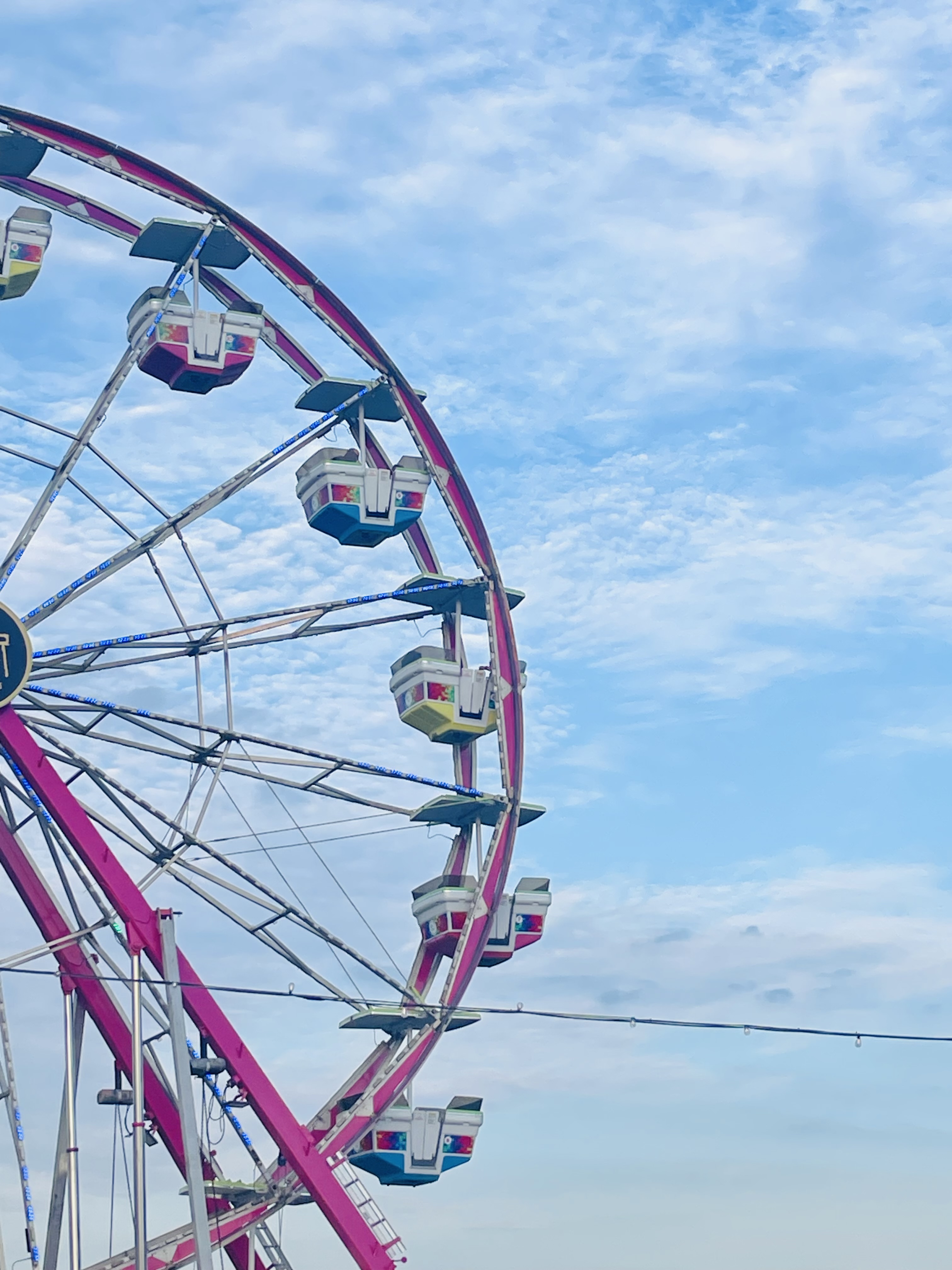 A pink ferris wheel against a light blue sku with fluffy clouds.