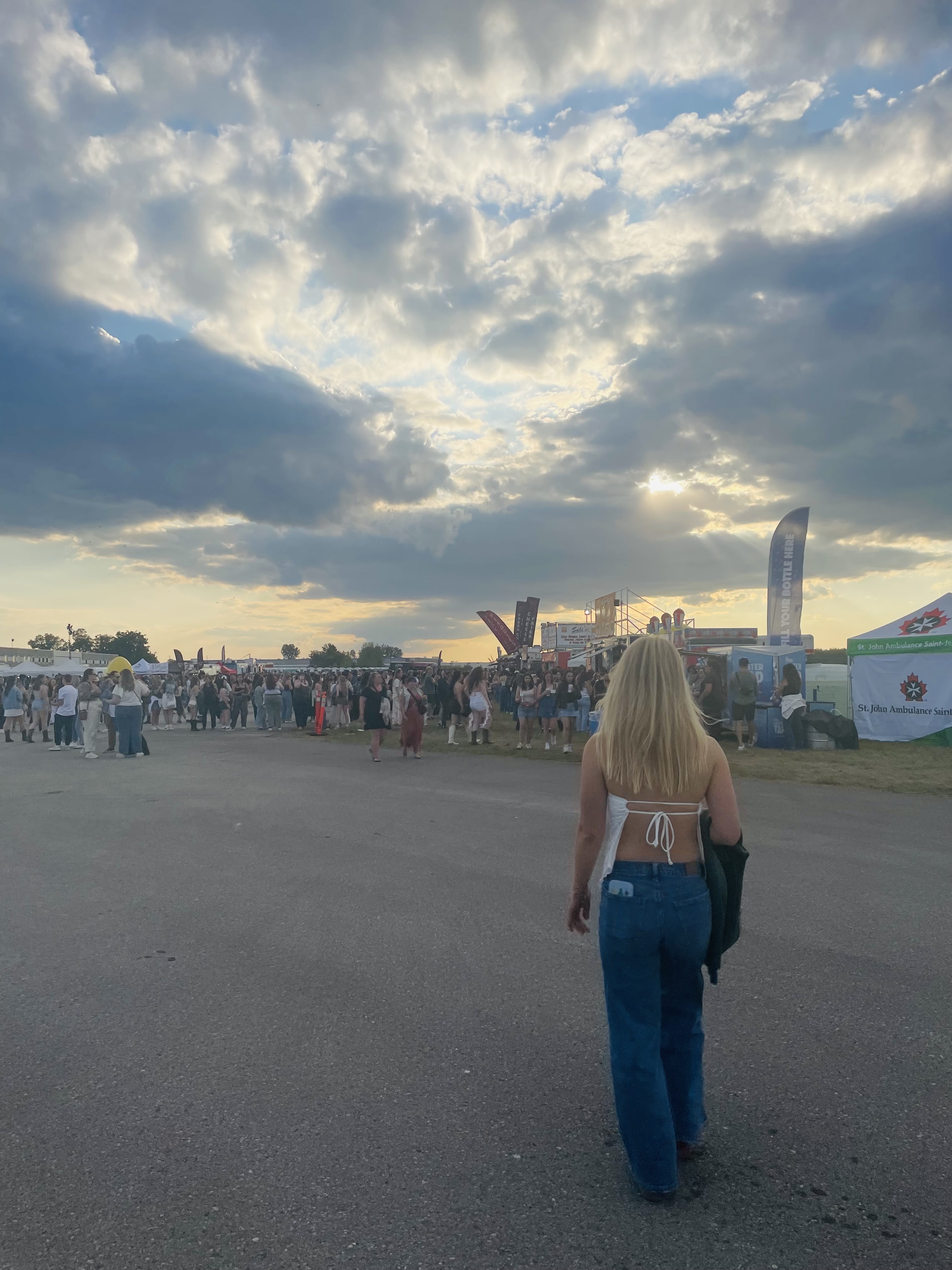 A girl with blonde hair wearing blue jeans walking towards a crowd of people at a music festival.