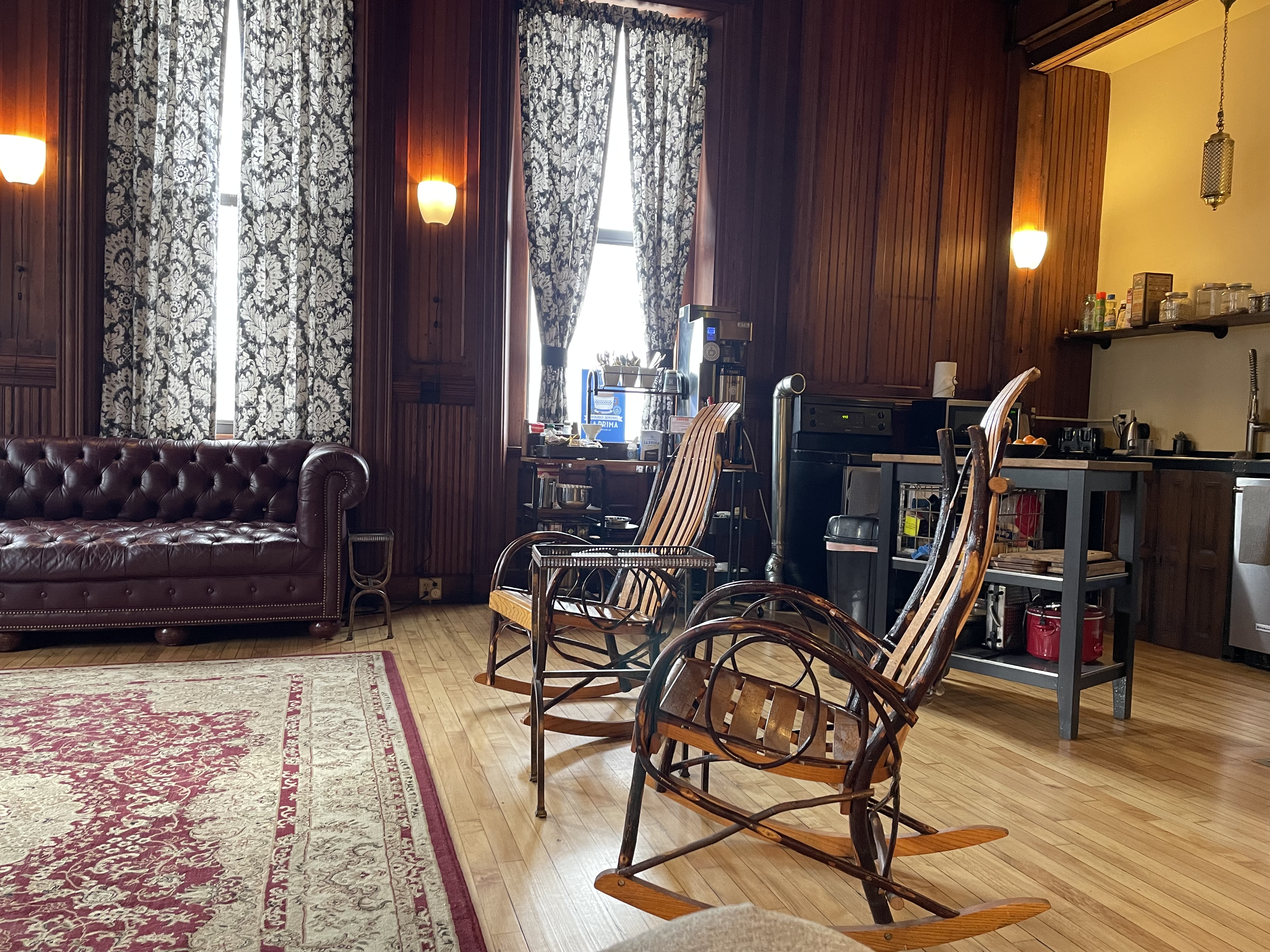 A set of ornate wood rocking chairs in an old wooden lobby with warm vintage lights.