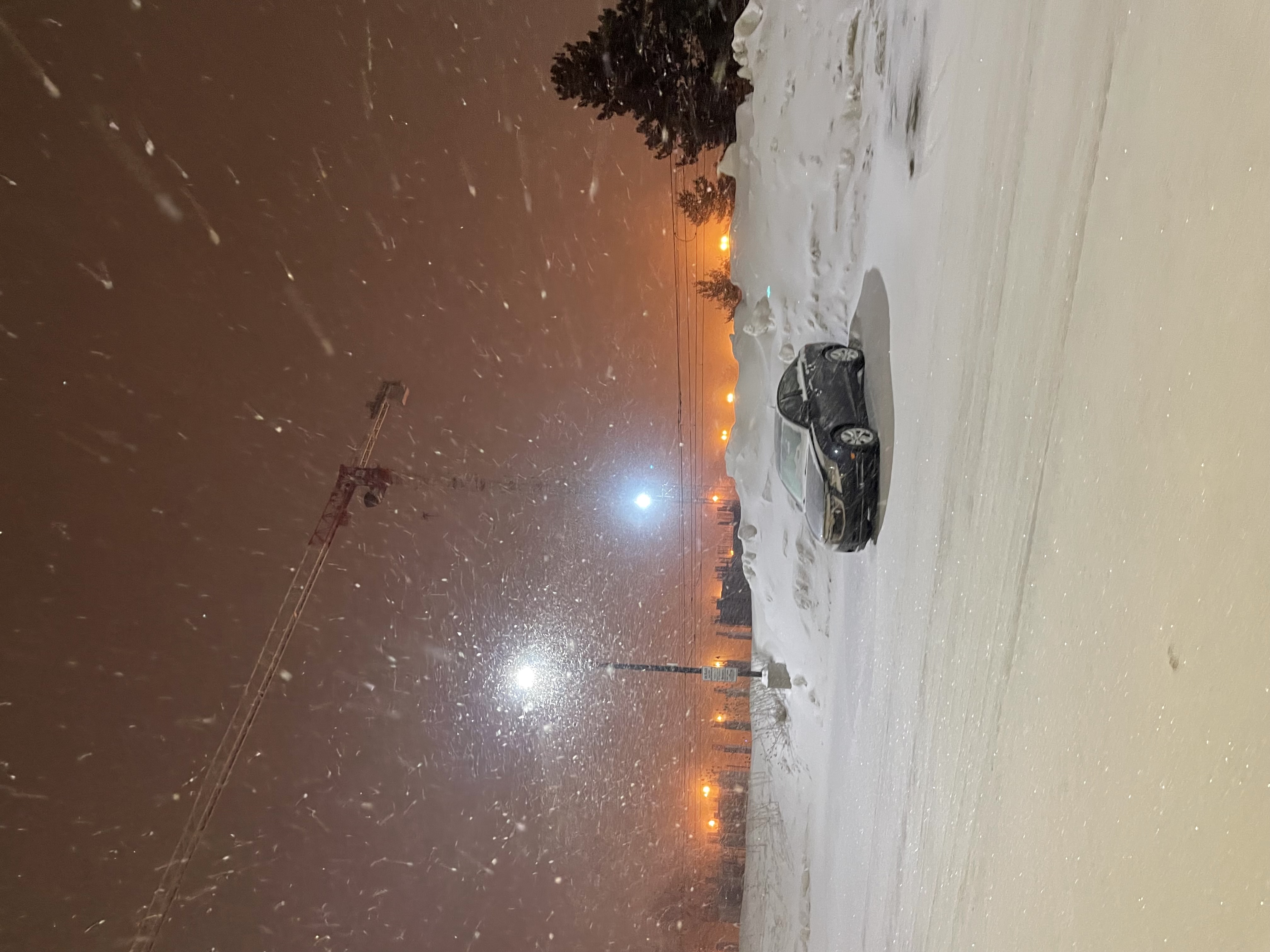 A lone black car in an empty snowy parking lot with orange sky behind.
