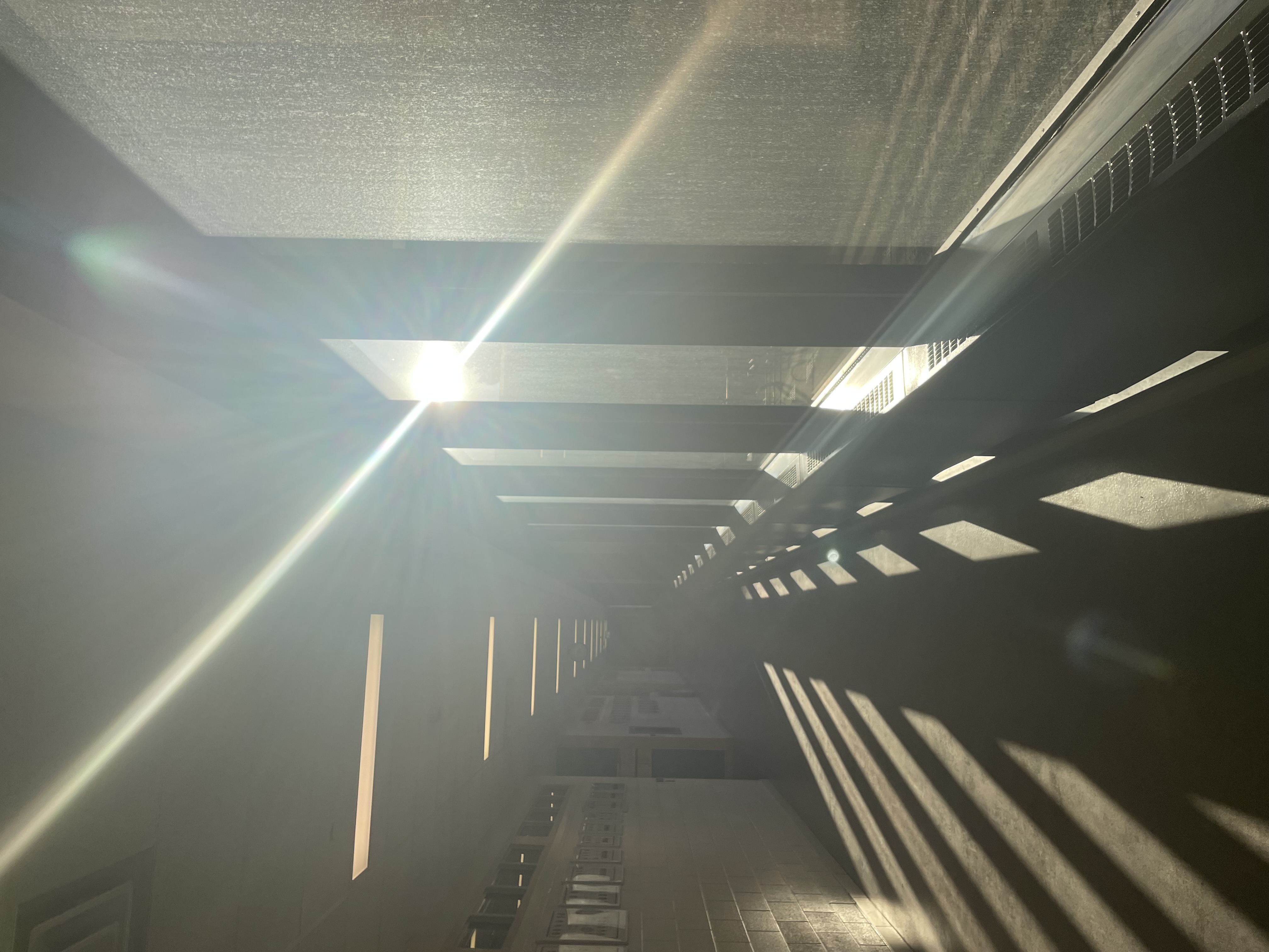 A dark hallway with big windows and bright sunlight streaming through the windows.
