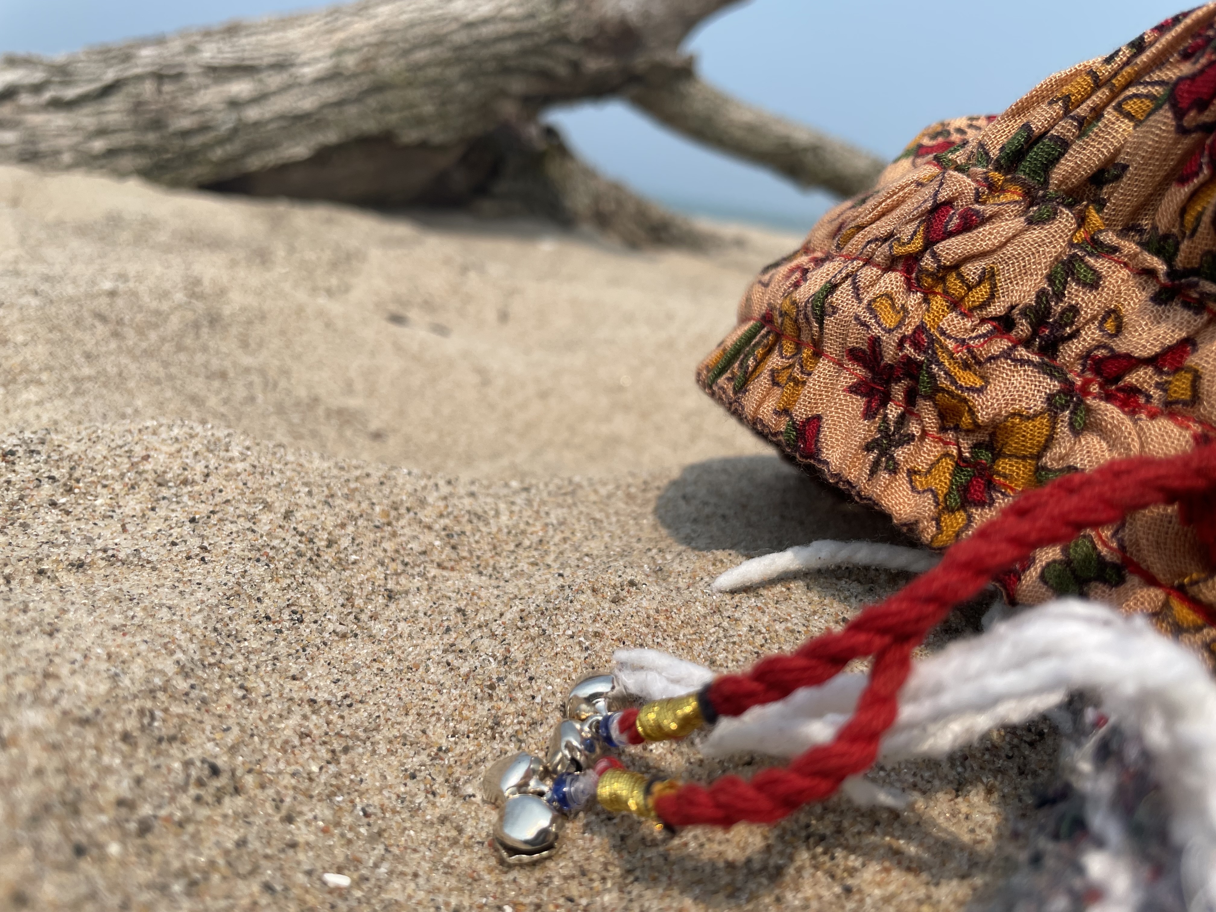 A piece of colourful fabric with a silver bell draped over a sandy beach with a low, hazy sun in the background.