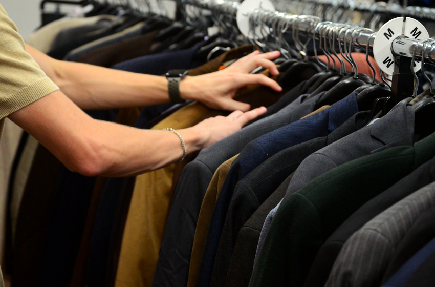 Hands sifting through nice suit jackets at a thrift store.